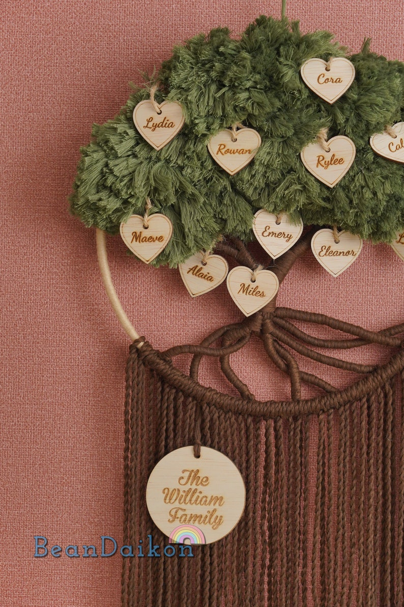 May include: A green yarn tree with brown yarn roots and a wooden circle with the text "The William Family" hanging from the bottom.  The tree is decorated with wooden hearts with names written on them, including Cora, Lydia, Rowan, Cal, Rylee, Emery, Eleanor, Maeve, Alaia, and Miles.