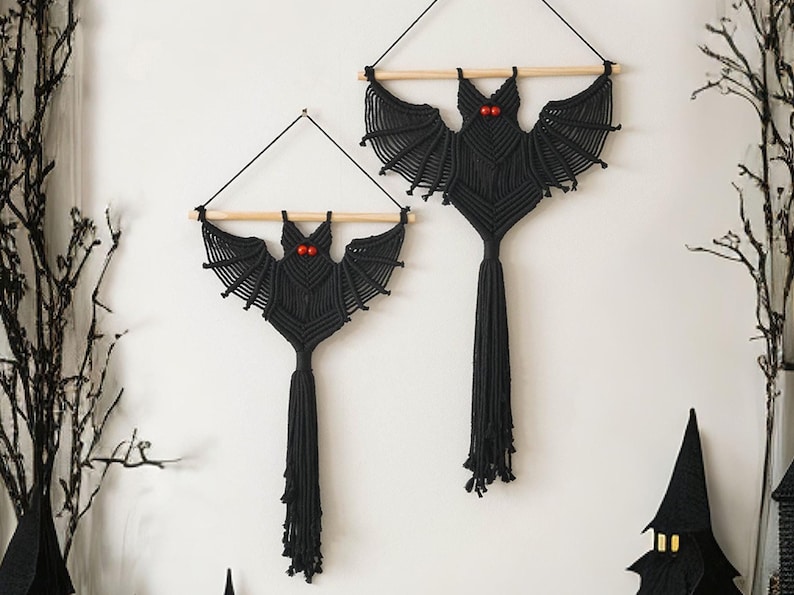 Puede incluir: Dos tapices de pared de murci&eacute;lago de macram&eacute; negro con ojos de cuentas rojas. Los murci&eacute;lagos cuelgan de listones de madera y tienen largas borlas.