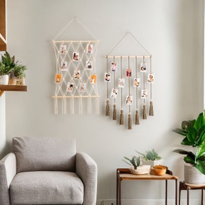 K&ouml;nnte beinhalten: Zwei Makramee-Wandbeh&auml;nge mit Holzleisten und Quasten. Der linke Wandbehang ist wei&szlig; und hat ein Gittermuster mit daran befestigten Fotos. Der rechte Wandbehang ist braun und hat ein kaskadierendes Design mit daran befestigten Fotos.