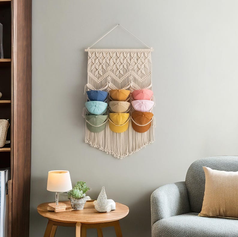 May include: A macrame wall hanging with a geometric pattern, featuring eight slots for storing hats. The slots are filled with colorful hats in shades of blue, green, yellow, orange, and pink.