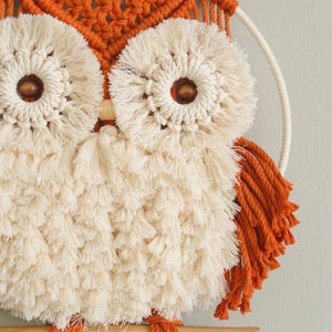 Peut inclure: Une suspension murale en macram&eacute; en forme de hibou avec une baguette en bois, dans un sch&eacute;ma de couleurs brun et blanc. Le hibou a de grands yeux ronds avec une frange blanche et un centre brun. Le corps du hibou est fait de frange blanche et les ailes sont faites de frange brune.