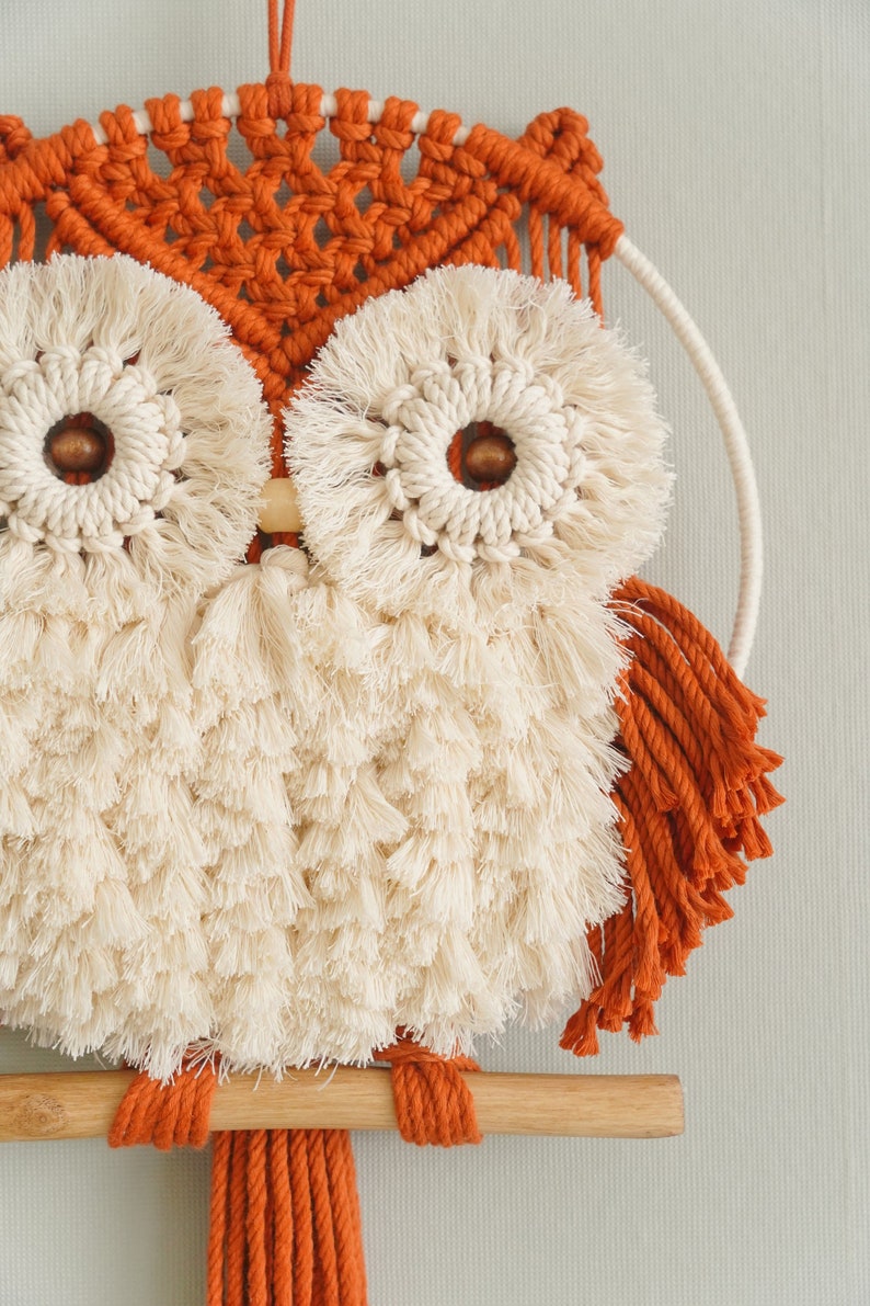 Peut inclure: Une suspension murale en macram&eacute; en forme de hibou avec une baguette en bois, dans un sch&eacute;ma de couleurs brun et blanc. Le hibou a de grands yeux ronds avec une frange blanche et un centre brun. Le corps du hibou est fait de frange blanche et les ailes sont faites de frange brune.