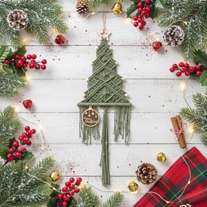 May include: A sage green macrame wall hanging shaped like a Christmas tree, featuring a wooden star at the top, small wooden beads along the sides, and a round wooden ornament with the text Merry Christmas hanging from the bottom.
