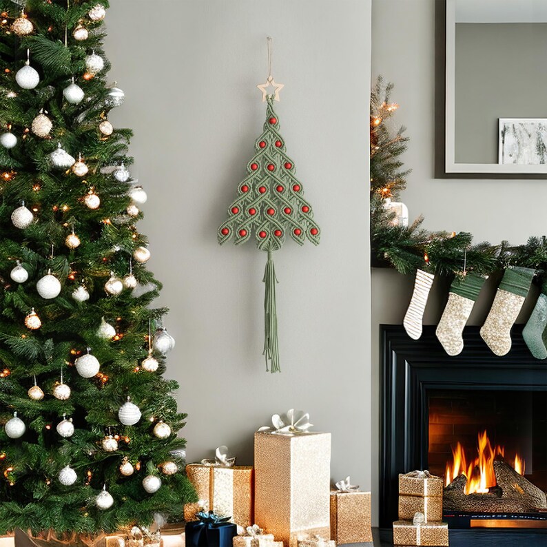 K&ouml;nnte beinhalten: Ein gr&uuml;ner Makramee-Weihnachtsbaum-Wandbehang mit roten Pompons und einem Holzstern an der Spitze. Der Baum h&auml;ngt an einer wei&szlig;en Wand mit einem Kamin und einem Weihnachtsbaum im Hintergrund.