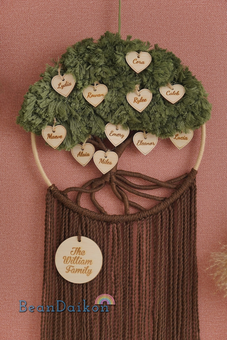 May include: A green and brown family tree wall hanging with wooden hearts featuring names like Cora, Rowan, Rylee, Caleb, Lucia, Emery, Eleanor, Maeve, Alaia, and Miles. The bottom of the hanging features a round wooden sign with the text "The William Family".