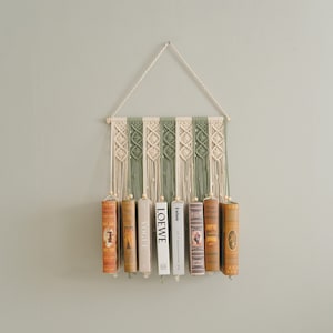 May include: A macrame wall hanging with a green and white pattern holds a row of books. The books have titles like "LOEWE" and "Vogue".