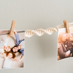 Peut inclure: Deux photos sont accroch&eacute;es &agrave; un mur blanc avec une corde blanche. La photo de gauche montre une famille de trois personnes allong&eacute;es sur le sol, souriant et se tenant la main. La photo de droite montre une femme et deux enfants qui s'embrassent dans un parc.