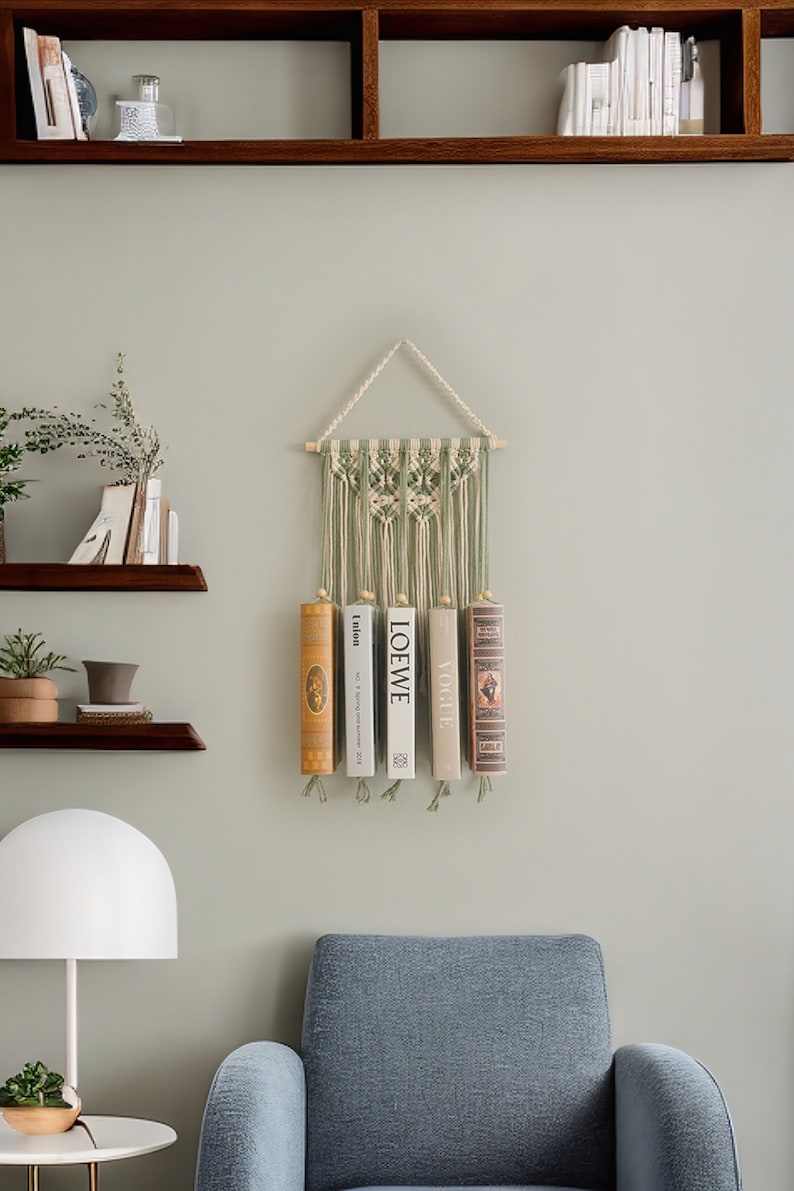 May include: A green and white macrame wall hanging with a wooden dowel at the top. Three books are hanging from the bottom of the macrame, with the titles "LOEWE", "VOGUE", and "talton" visible.