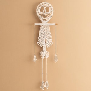 May include: White macrame wall hanging with a peace sign design and tassels. The hanging is made of cotton cord and has a wooden dowel at the top.