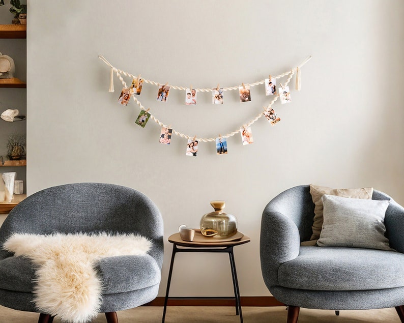 Peut inclure: Deux fauteuils gris avec des jet&eacute;s en fausse fourrure blanche et un coussin marron, face &agrave; face dans un salon. Une petite table noire avec un vase en verre dor&eacute; se trouve entre les fauteuils. Une guirlande de photos est accroch&eacute;e au mur au-dessus de la table.