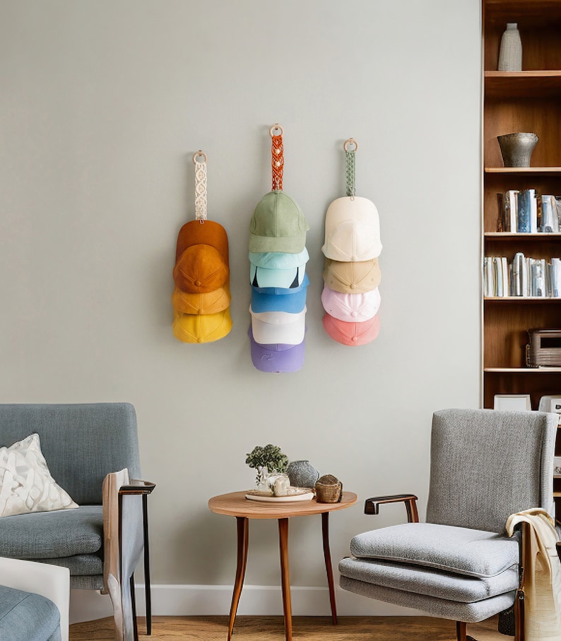 May include: Three wall-mounted hat organisers, each holding a stack of baseball caps in various colours. The caps include shades of yellow, orange, green, blue, pink, and purple. The organisers have decorative hanging straps.