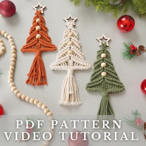 以下が含まれることがあります： オレンジ、白、緑の3つのマクラメ製のクリスマスツリーオーナメント。木製ビーズと星が付いています。オーナメントは、木製ビーズのガーランドと赤いクリスマスオーナメントのある白い背景に吊り下げられています。