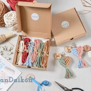 May include: A craft kit for making macrame heart keychains. The kit includes five different colors of string, wooden heart charms, key rings, and instructions. The kit is packaged in a brown cardboard box.