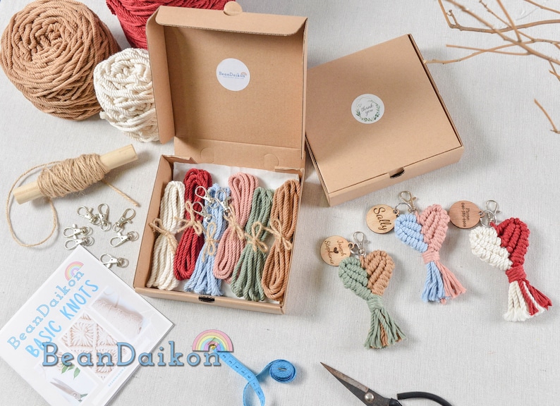 May include: A craft kit for making macrame heart keychains. The kit includes five different colors of string, wooden heart charms, key rings, and instructions. The kit is packaged in a brown cardboard box.