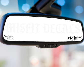 May include: A black car rearview mirror featuring a white decal with the text MISFIT DECALS in the center. The words left and right are printed in a gothic font at the bottom corners, each accompanied by a small black bat silhouette graphic.