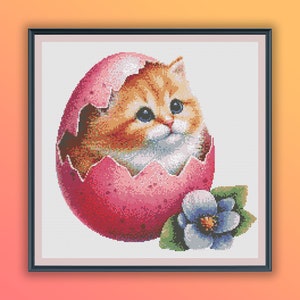 Puede incluir: Un lindo gatito naranja y blanco asoma de un huevo rosa roto con una flor azul a su lado.