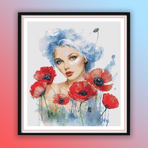 Op de afbeelding: Een ingelijst borduurwerk met kruissteek, met een vrouw met blauw haar en rode klaprozen. Het gezicht van de vrouw is zichtbaar en ze is omringd door rode klaprozen met groene stelen.