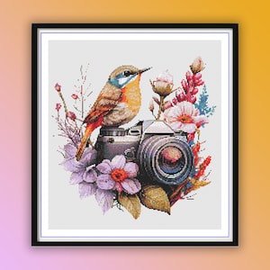 Puede incluir: Un pájaro colorido posado en una cámara vintage rodeada de flores. El pájaro es naranja, azul y marrón. La cámara es negra y plateada. Las flores son moradas, rosas, blancas y verdes.