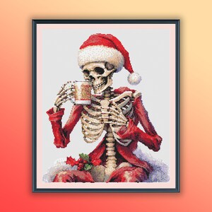 以下が含まれることがあります： 赤いサンタの服を着てサンタの帽子をかぶった骸骨が、ホットチョコレートの入ったマグカップを持っています。骸骨は白いふわふわの表面に座っています。