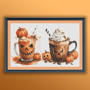 May include: Cross-stitch art featuring two mugs of pumpkin spice lattes with jack-o'-lantern faces. One mug has whipped cream and a straw. Small pumpkins and fall leaves surround the mugs, creating a festive Halloween theme.