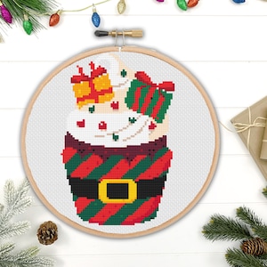 May include: A cross-stitch pattern of a Christmas cupcake with red and green stripes, a brown belt, and white frosting topped with red and green presents.