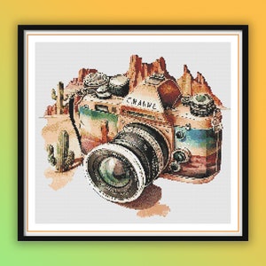 Puede incluir: Una cámara vintage con un diseño estampado en marrón, azul y rojo, sobre un fondo de paisaje desértico con cactus.