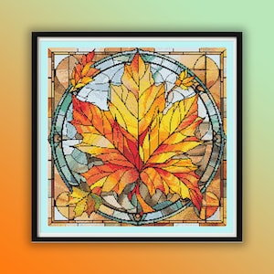 Puede incluir: Un diseño de vitral con una gran hoja de arce naranja, amarilla y roja en un marco circular. El marco está hecho de vidrio azul, verde y marrón.