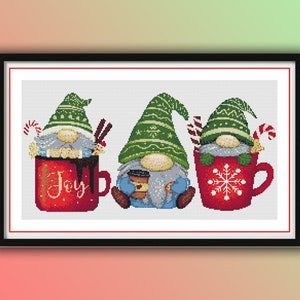 May include: Three gnomes wearing red and white Santa hats are sitting in mugs. The mug on the left says "Joy" and has a chocolate swirl. The middle gnome is holding a cup of coffee. The mug on the right has a snowflake design.