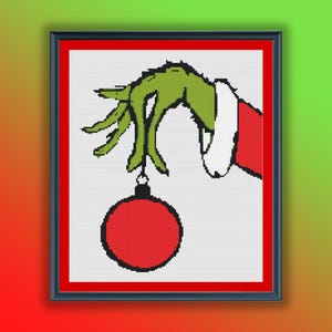 Puede incluir: Una mano verde con una manga roja y blanca sosteniendo una bola de Navidad roja.