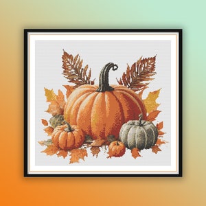 May include: A cross-stitch pattern featuring a still life of pumpkins and autumn leaves. The pumpkins are orange and gray, and the leaves are in shades of brown, orange, and yellow.