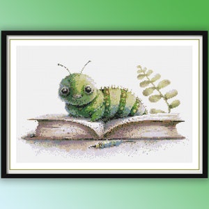 Può includere: Un bruco verde con occhi grandi è seduto su un libro chiuso con una foglia verde dietro.