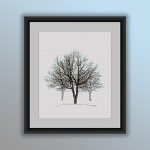 Op de afbeelding: Ingelijste kunstdruk met een winterlandschap. Het kunstwerk toont drie kale bomen tegen een witte achtergrond, wat een besneeuwde scène suggereert. De bomen zijn weergegeven in grijstinten en bruin, met gedetailleerde takken.
