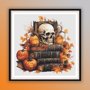 Op de afbeelding: Een kruissteekpatroon met een schedel, pompoenen en boeken. De schedel is omringd door herfstbladeren en de boeken zijn op elkaar gestapeld. De kleuren zijn voornamelijk bruin, oranje en wit.