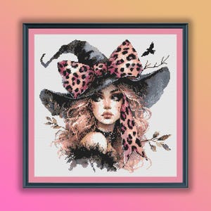May include: A cross-stitch pattern featuring a witch with pink and black leopard print bow on her hat. The witch has long blonde hair and is wearing a black hat with a wide brim.
