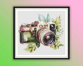 May include: A vintage camera with a green and brown finish, surrounded by green leaves. The camera has a large lens and a viewfinder.