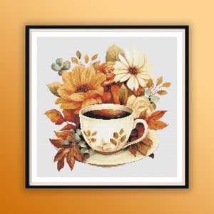 Op de afbeelding: Een wit theekopje en schotel met een bloemenmotief, gevuld met bruine koffie, omringd door een boeket van oranje, gele en witte bloemen met groene bladeren.