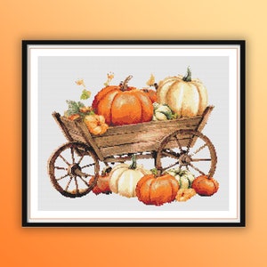 May include: A cross-stitch design featuring a wooden cart overflowing with pumpkins. The pumpkins vary in size and color, ranging from orange to white. The cart has large wooden wheels and is set against a white background.