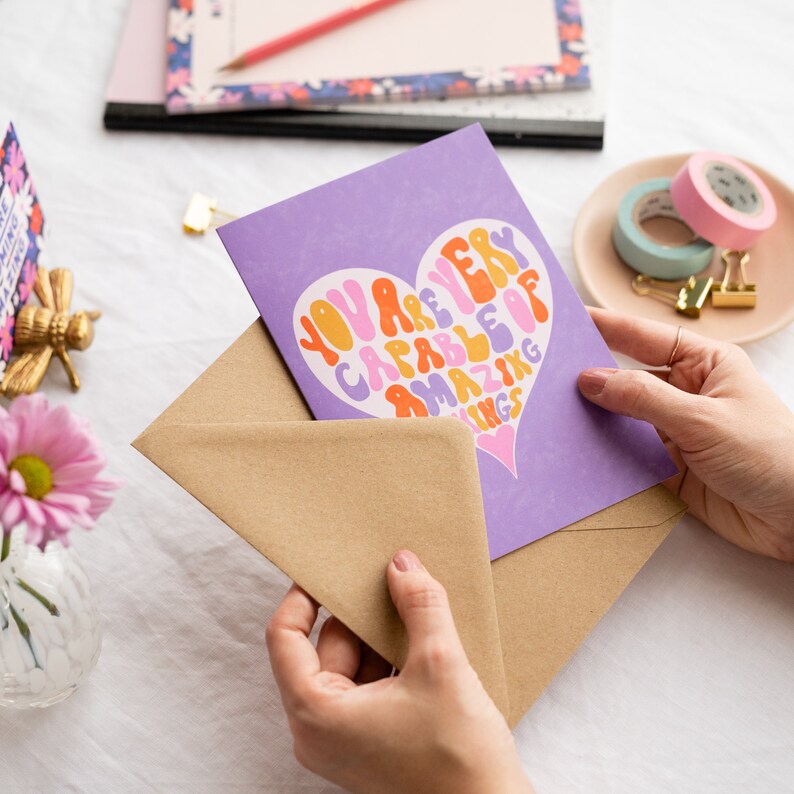 May include: A purple card with a heart-shaped design that says "You are very capable of amazing things". The card is in a brown envelope.