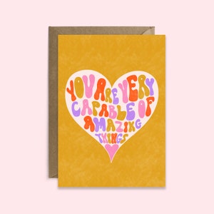 May include: A yellow card with a pink heart shape containing the text "You are very capable of amazing things" in a colorful, retro font.