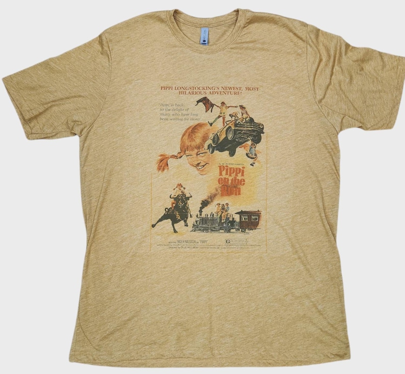 Op de afbeelding: Een beige crew neck t-shirt met een vintage filmposter ontwerp. De poster toont Pippi Langkous met de tekst "Pippi on the Run" en andere tekst. Het shirt is gemaakt van een zacht materiaal.