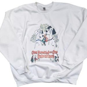 May include: White crew neck sweatshirt with a graphic from the Disney film "One Hundred and One Dalmatians." The design features two Dalmatians, a human character, and the film's title. The sweatshirt is a classic style.