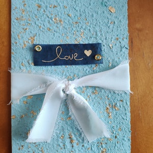 Invito A5 grande ed elegante di colore azzurro in carta fatta a mano con intarsio in foglia oro chiuso con un nastro