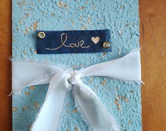 Large elegant light blue A5 invitation in handmade paper with gold leaf inlay closed with a ribbon