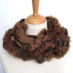 May include: A brown and green velvet and silk scarf with a ruffled edge and pom-poms.