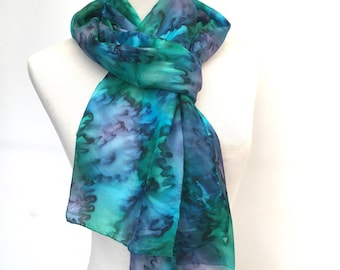 Zijden sjaal in rijke blauw- en groentinten met een vleugje paars. 180 cm lang, met de hand beschilderd in pauwkleuren met een afwerking met watereffect.