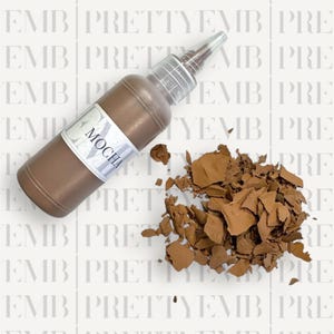 May include: A brown bottle of paint with a white label that says "Mocha". The bottle is tipped over and the paint is spilling out onto a white surface.