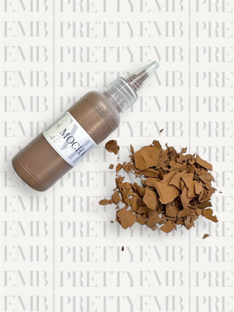 May include: A brown bottle of paint with a white label that says "Mocha". The bottle is tipped over and the paint is spilling out onto a white surface.