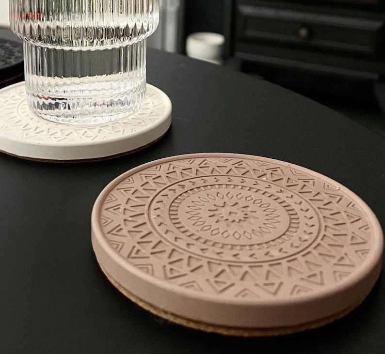 Puede incluir: Dos posavasos redondos, uno blanco y otro marr&oacute;n claro. El posavasos marr&oacute;n tiene un patr&oacute;n geom&eacute;trico con un dise&ntilde;o en relieve.
