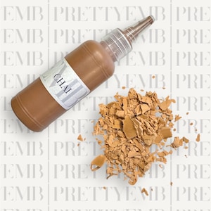 May include: A brown bottle of liquid paint with a white label that says "CHAI". The bottle is lying on a white surface with a pile of broken brown paint chips.