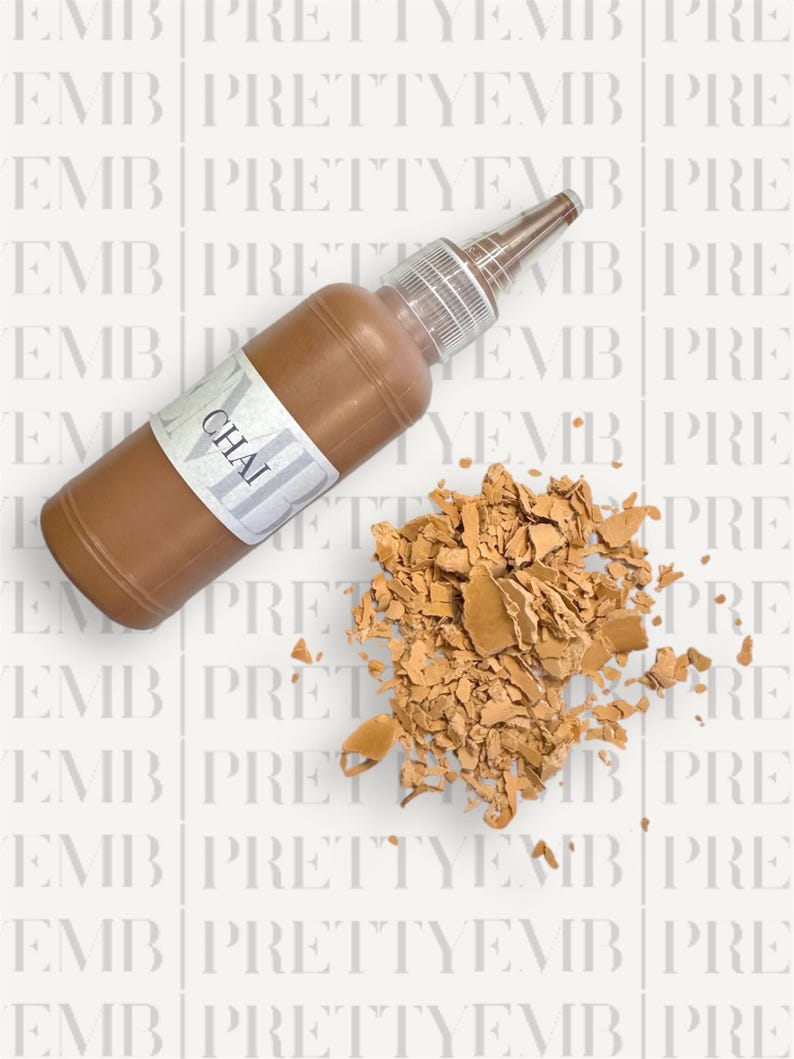 May include: A brown bottle of liquid paint with a white label that says "CHAI". The bottle is lying on a white surface with a pile of broken brown paint chips.